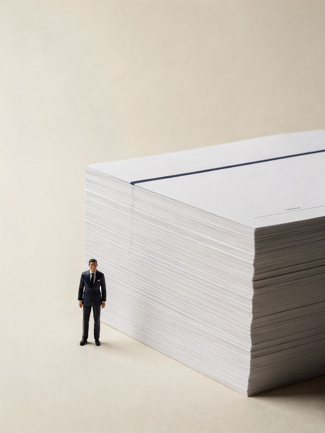 A tiny suited figurine standing beside a monumental, perfectly squared stack of white documents